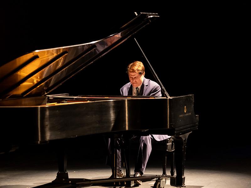 Man in suit on stage playing a piano